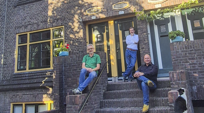 De twee bewoners, Henk-Jan van Vulpen (rechts op de foto) en Karel Kalis (midden), van de nummers 65 en 65bis, hebben ieder hun woning met aandacht voor het oorspronkelijke karakter en historische details onderhouden en hersteld. Van Vulpen: “We ontdekten dat de kleur op de kozijnen en deuren, wit en groen, anders is dan toen de huizen in de jaren twintig werden gebouwd. Waarom is dat veranderd? Mogelijk omdat het goedkoper was? Of in de jaren zeventig beter paste bij de smaak? In ieder geval is het gedaan door de woningbouwvereniging, voordat de woningen in 1974 verkocht werden, meestal aan de zittende huurders. Andrea Klerks vertelt: “Voor onderzoek naar de oorspronkelijke kleurstelling kun je gebruikmaken van oude bronnen, zoals bouwtekeningen en foto’s, en van stratigrafisch onderzoek, dat is het krabben in verflagen. Gelukkig hadden we hier veel materiaal voor beide vormen van onderzoek.” Zo konden ze tot een duidelijke kleurbepaling komen: okergeel voor de kozijnen en rijtuig-groen voor het hout van de ramen en voor de deuren. Voorbeeld Ondanks dat ermee de eenheid in kleurafwerking van de vijf bouwblokken doorbroken wordt, adviseert Erfgoed de gemeente positief te reageren op de vergunningaanvraag. Dat er voor één huis vergunning is verleend, is heel uitzonderlijk. Andrea: “Dat kon omdat het om het eerste huis gaat, aan de rand van het eerste blok. Het is daarmee een goed voorbeeld van het positieve effect op de uitstraling van de gevel geworden.” Er ontsnapt Karel Kalis een kleine zucht als hij beschrijft wat er allemaal bij komt kijken om zo’n plan te realiseren. “Het helpt dat ik door mijn werk veel relevante kennis hierover heb. Dat ik weet hoe je een vergunning aanvraagt en op welke gemeentelijke en landelijke subsidiepotjes je een beroep kunt doen. En bovendien glasleveranciers en schilders ken bij wie dit precieze werk in goede handen is.” In mei dit jaar is het zover: het huis staat te glimmen in zijn nieuwe, oude kleuren. Dan is het tijd voor een ‘open trapmoment’: buurtbewoners worden uitgenodigd om te komen kijken. Van Vulpen: “De reacties varieerden van ’helemaal niet mooi’ tot superenthousiast. Wij blijven er graag buiten of het al of niet mooi is, het gaat ons erom dat het de oorspronkelijke kleurstelling is.” Blok 5 Hilde Krol raakte geïnteresseerd door die uitnodiging. In eerste instantie vond zij het vreemd dat bij één woning zulke andere kleuren gebruikt konden worden. Tot ze de achtergrond kende, dat veranderende het beeld en maakte haar enthousiast. Zij woont in de Trompstraat, in het kleinste blok in deze stijl, blok 5 op de bouwtekeningen. Haar buren herkennen de overwegingen – van verbazing naar enthousiasme – en overwegen samen op termijn ook het schilderwerk in de oude kleuren te herstellen. Dat hun blok ‘maar’ zes woningen heeft, kan hierbij een voordeel zijn. De onderzoekers van het eerste uur staan klaar om hun kennis en adviezen te delen. Andrea: “Bij het aanvragen van een vergunning helpt het enorm als je dat als groep buren van aansluitende huizen doet, zowel voor de kosten als voor de snelheid van de procedure.” Van Vulpen en Kalis maken geïnteresseerden graag wegwijs in alles wat zij onderweg hebben geleerd. Andrea Klerks: “Herstel in de oorspronkelijke kleurstelling doet de schoonheid van de huizen extra spreken. En eenheid van kleur maakt dat andere ontstane verschillen, in bijvoorbeeld de voegen of deuren en ramen, veel minder in het oog springen.” Lees ook het verhaal van het kleurherstel op Erfgoed Utrecht. [kader] Amsterdamse School in Zeehelden De Zeeheldenbuurt is rond 1900 ontstaan en kenmerkt zich door statige herenhuizen. De woningbouwvereniging Trio, die zich richtte op onder meer het middenkader van de Nederlandse Spoorwegen (het NS-hoofdkantoor had zich in Utrecht gevestigd) liet in de periode 1921-22 vijf woonblokken bouwen, ontworpen door architect Albert Kool en ingenieur A. van Rood. Deze blokken zijn gebouwd in de Amsterdamse Schoolstijl. Typische kenmerken van deze stijl zijn: het expressieve en plastische metselwerk, uitstekende en terugliggende gevelvlakken, die als één geheel de hoek omgaan, bijzondere raamvormen, een bepaalde kleurstelling, karakteristieke hekjes (de Amsterdamse school richtte zich op de vormgeving van de héle buitenruimte), brede trappen (ze leiden naar twee voordeuren voor de benedenwoningen en twee voor de bovenwoningen), platte daken en erkers boven de entrees. Ook kenmerkend is dat niet ieder huis een afzonderlijk object is, maar dat het gaat om het hele blok als compositie. Het is zeker de moeite waard om met deze kennis de blokken een keer te bekijken. Het gaat hierbij om de Admiraal van Gentstraat 41-65, Van Brakelstraat 9-23 (het metselwerk en de hekjes), M.H. Trompstraat 13-15 (vele kleine details) en Admiraal van Gentstraat 10-16. In 1987 kregen de huizen de status van gemeentelijke monument. Voor wijzigingen in het gevelbeeld is een vergunning nodig, ook voor het terugbrengen naar de oorspronkelijke kleurstelling. Een leuk weetje is dat de bakstenen niet zomaar gekozen zijn. Bij de bouw werden partijen stenen gebruikt die waren afgekeurd of overgebleven bij de bouw van De Inktpot, het hoofdkantoor van de NS aan het Moreelsepark.